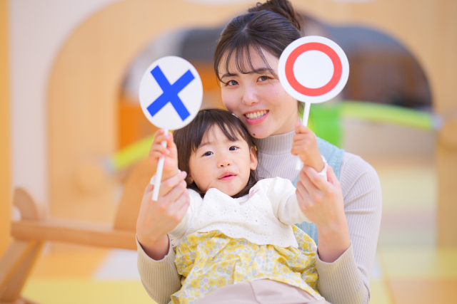 ◯・✕の札をもつ保育士と子ども