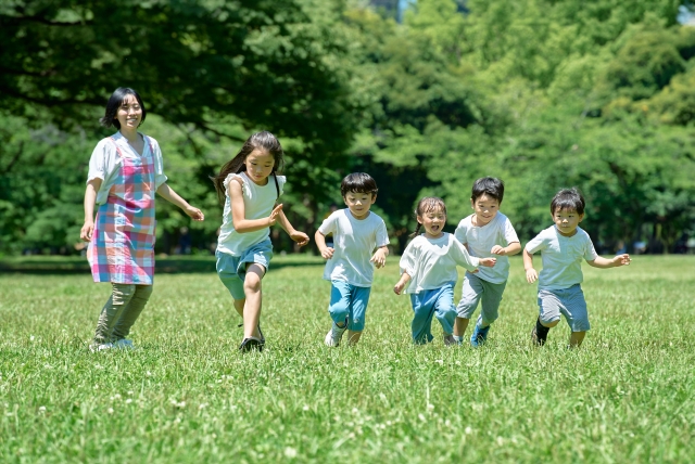 保育士と一緒に芝生の上を駆け回る子どもたち