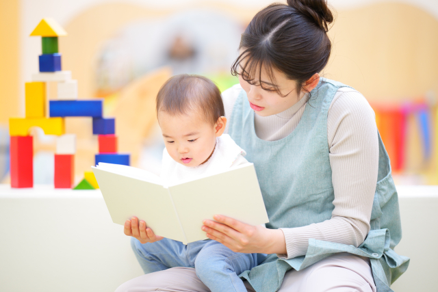 赤ちゃんに絵本を読む女性保育士