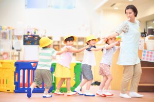 保育士と幼児たちが並んでつながり電車ごっこ